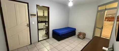 A compact room with a bed, a desk, a ceiling fan, and a door leading to a bathroom.