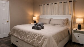 A neatly made bed with a white headboard, two bedside lamps, and a rolled towel on the bed.