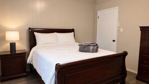 A bedroom with a wooden bed, a nightstand with a lamp, a door, and a dresser.