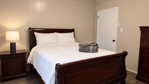 A bedroom with a wooden bed, a nightstand with a lamp, a door, and a dresser.