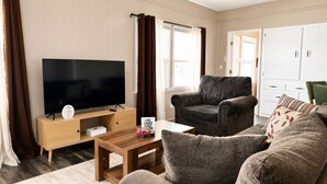 A living room with a flat-screen TV, a dark armchair, a sofa, and a wooden coffee table.