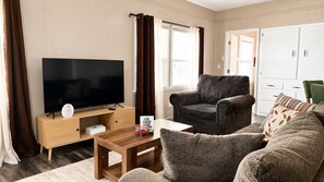 A living room with a flat-screen TV, a dark armchair, a sofa, and a wooden coffee table.