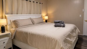 A neatly made bed with a headboard, two bedside lamps, a folded towel on the bed, and a nightstand with a drawer. - Cozy 2BR Home with King Bed + In-Unit Laundry (Lemoore)