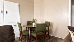 A dining area with a round table, four green upholstered chairs, a potted plant, and a white cabinet.