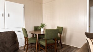 A dining area with a round table, four green upholstered chairs, a potted plant, and a white cabinet.