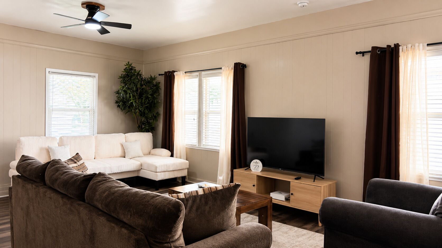A living room with a sectional sofa, a flat-screen TV, a coffee table, and a plant.