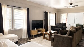 A modern living room with a flat-screen TV, sofas, a coffee table, and a ceiling fan.