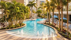 A swimming pool with a fountain, surrounded by palm trees and lounge chairs, with a building in the background. - Beachfront Marriott Crystal Shores Resort + Resort Amenities Included (Marco Island)