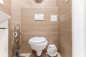 Un baño moderno con inodoro, secamanos y cubo de basura.