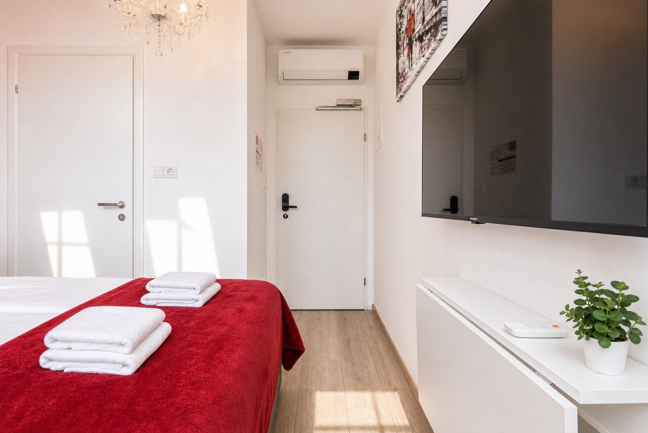Ett hotellrum med en säng, ett skrivbord, en växt och en tv.