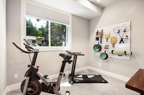 Ein Heimfitnessraum mit zwei Ergometer, einem Wand-Trainingsgestell und einem Fenster mit Blick auf Grünflächen.