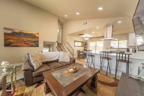 A spacious living area with a brown leather sofa, a coffee table, and a dining area with bar stools. - The Pearl · Backyard, Hot Tub & Park Next Door (Mesa)