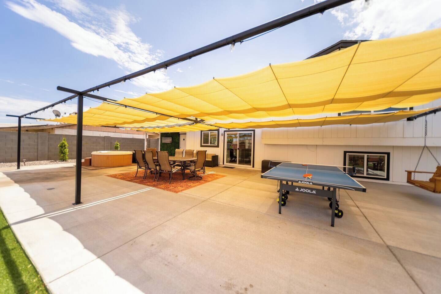 An outdoor patio area with a ping pong table, a table with chairs, and a hot tub.