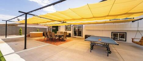 An outdoor patio area with a ping pong table, a table with chairs, and a hot tub.