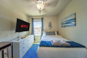 A hotel room with a bed, a desk with a television displaying 'NETFLIX', a window with curtains, and a painting on the wall. - The Pearl · Backyard, Hot Tub & Park Next Door (Mesa)