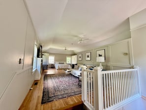 A hallway with a wooden floor, a white railing, and a ceiling fan.