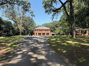 A two-story brick house with a garage, surrounded by a well-maintained lawn and trees.