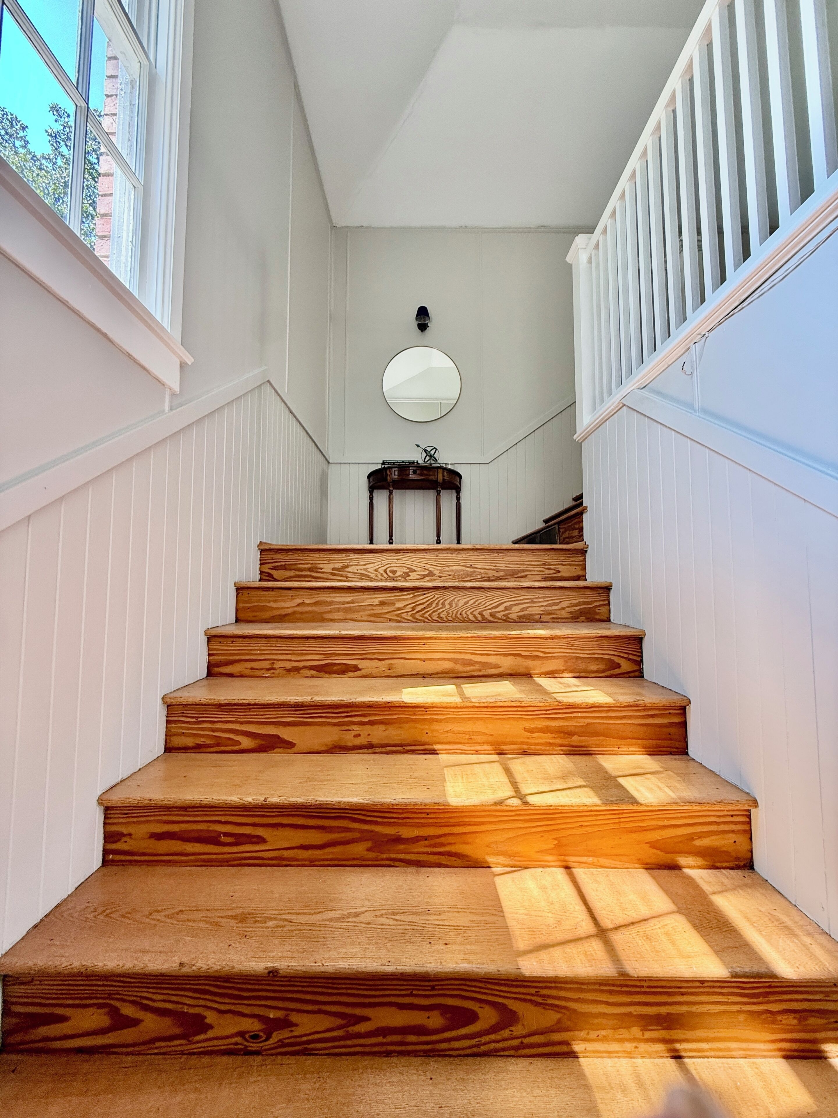 Un escalier en bois, avec des murs blancs et un miroir rond accroché au mur.