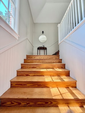 A wooden staircase with white walls and a round mirror on the wall.