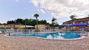 Una piscina amb gandules i ombrel·les, envoltada per un pati de maó i edificis al fons.