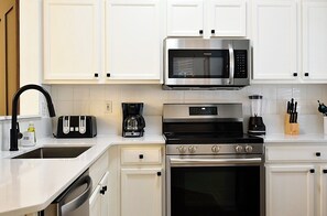 A modern kitchen with white cabinetry, a stainless steel microwave, a coffee maker, a toaster, and a stove. - Spacious 3-Bedroom TH Disney (Kissimmee)