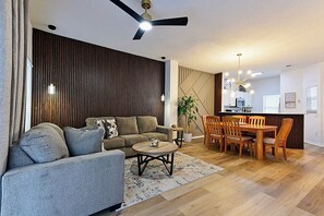 A modern living room with a sofa, coffee table, and dining area with chairs. - Spacious 3-Bedroom TH Disney (Kissimmee)
