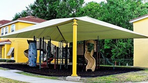 Un parc infantil amb un tobogan groc i elements per escalar, cobert per una gran marquesina.