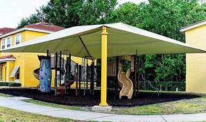 A playground with a yellow slide and climbing structures, covered by a large canopy. - Spacious 3-Bedroom TH Disney (Kissimmee)