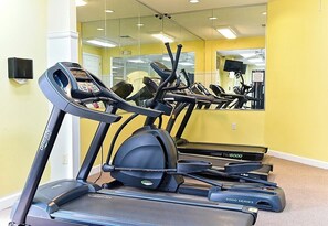 Ein Fitnessraum mit Laufbändern, Crosstrainern, einem Spiegel und einer gelben Wand.