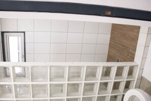 Casa de banho com sanita, espelho e parede revestida a azulejos.