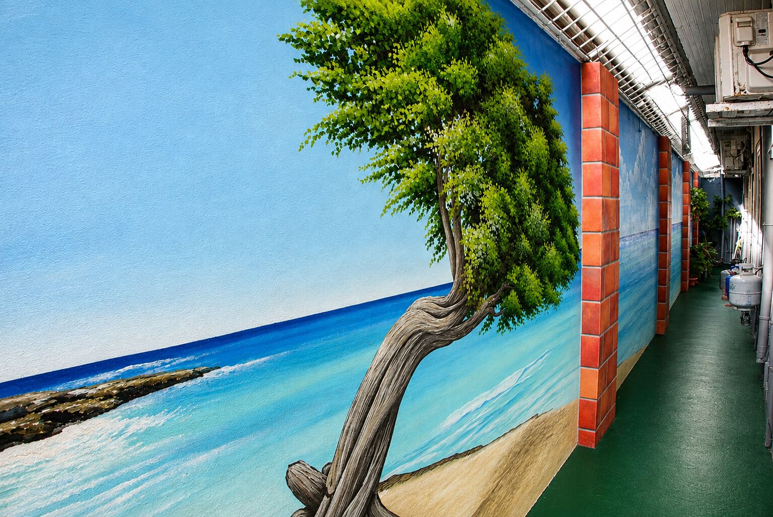 Un mural que representa una escena de platja amb un arbre, un cel blau clar i una mar tranquil·la.