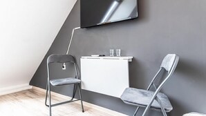 A modern room with a flat-screen TV mounted on the wall, a white desk with two glasses, and two foldable chairs.