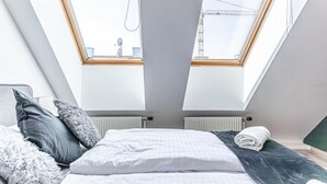 A bedroom with a skylight, a bed with pillows, and a radiator.