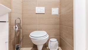 A small, modern bathroom with a toilet, a bidet, and a trash bin.