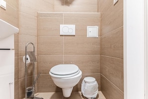 A small, modern bathroom with a toilet, a bidet, and a trash bin.
