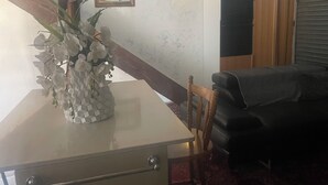 Une pièce comprenant une table à manger, un vase de fleurs, une chaise en bois, un canapé noir, une lampe fixée au mur et un tableau encadré.