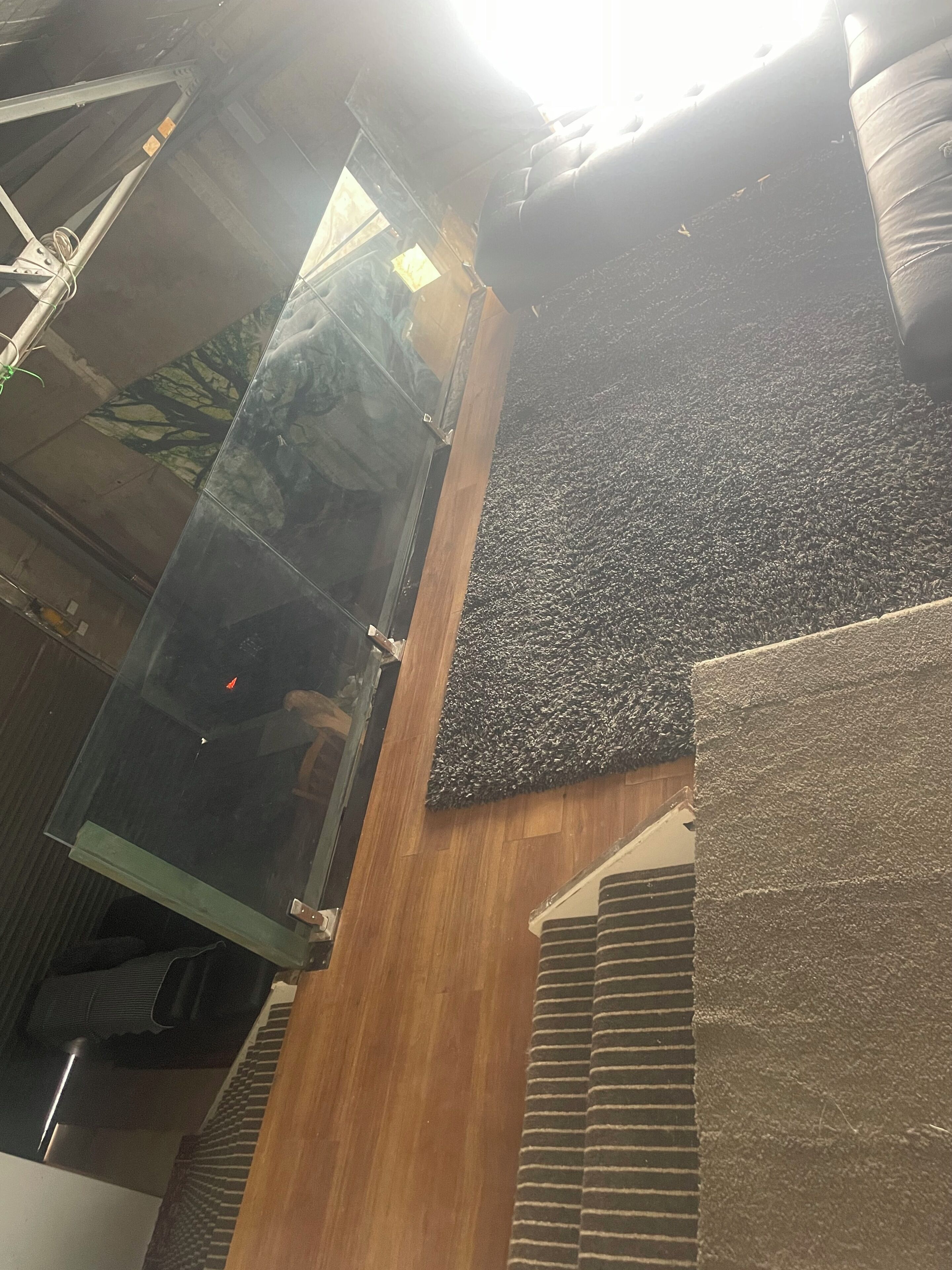 A modern interior with a glass elevator shaft, a textured wall, and a wooden floor.