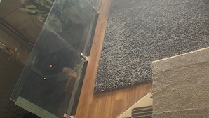 Un intérieur moderne avec un puits d’ascenseur en verre, un mur à texture et un plancher en bois.