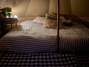 Een bed met hemel, een nachtkastje met een bordje en een geruit kleed.