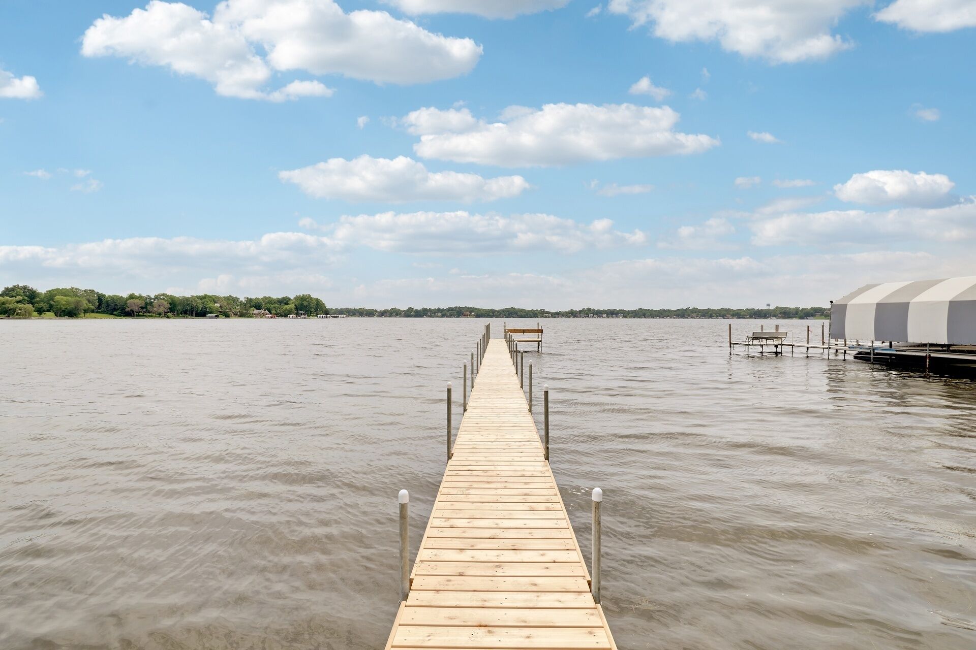 A wooden pier extending into calm water, leading to a bench and a white building on the right.
