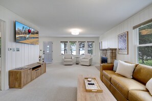 Ein Wohnzimmer mit Fernseher, Sitzgelegenheiten, Kamin und Blick ins Freie.