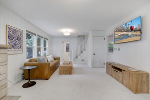Un hall d’entrée spacieux avec un escalier, un salon comprenant un canapé et une table basse, et un téléviseur fixé au mur.