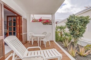 A patio with white plastic chairs and a table, a wooden door, and a small garden with plants. - Your Winter Home by the Sea with a Pool (Playa Honda)