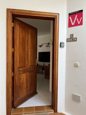 A wooden door leading into a room with a flat-screen TV, a small table, and a chair. - Your Winter Home by the Sea with a Pool (Playa Honda)