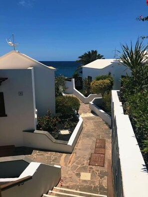 A narrow pathway leading to a coastal area with white buildings, stone steps, and a clear view of the sea. - Your Winter Home by the Sea with a Pool (Playa Honda)