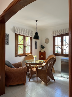 A dining area with wicker furniture, a glass table, and a hanging light fixture. - Your Winter Home by the Sea with a Pool (Playa Honda)