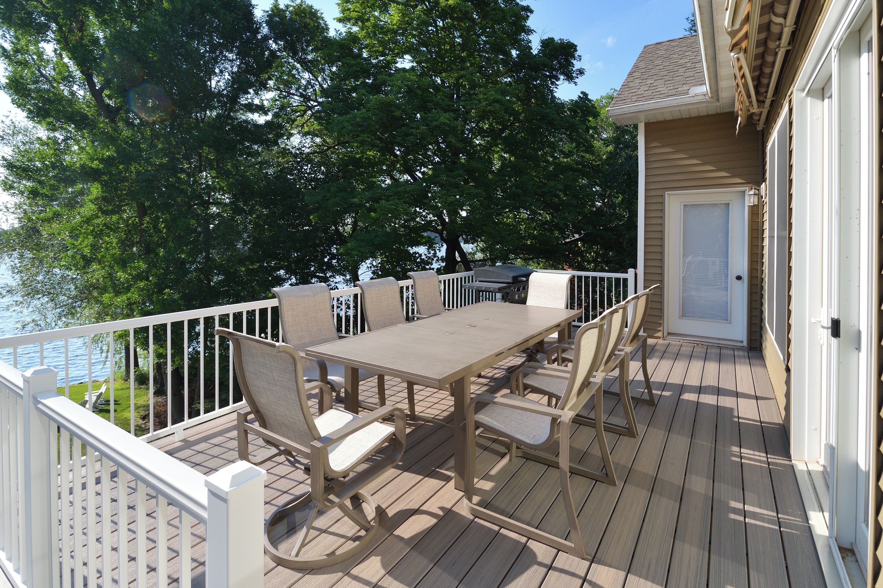 A wooden deck with a table and chairs, overlooking a body of water and trees.