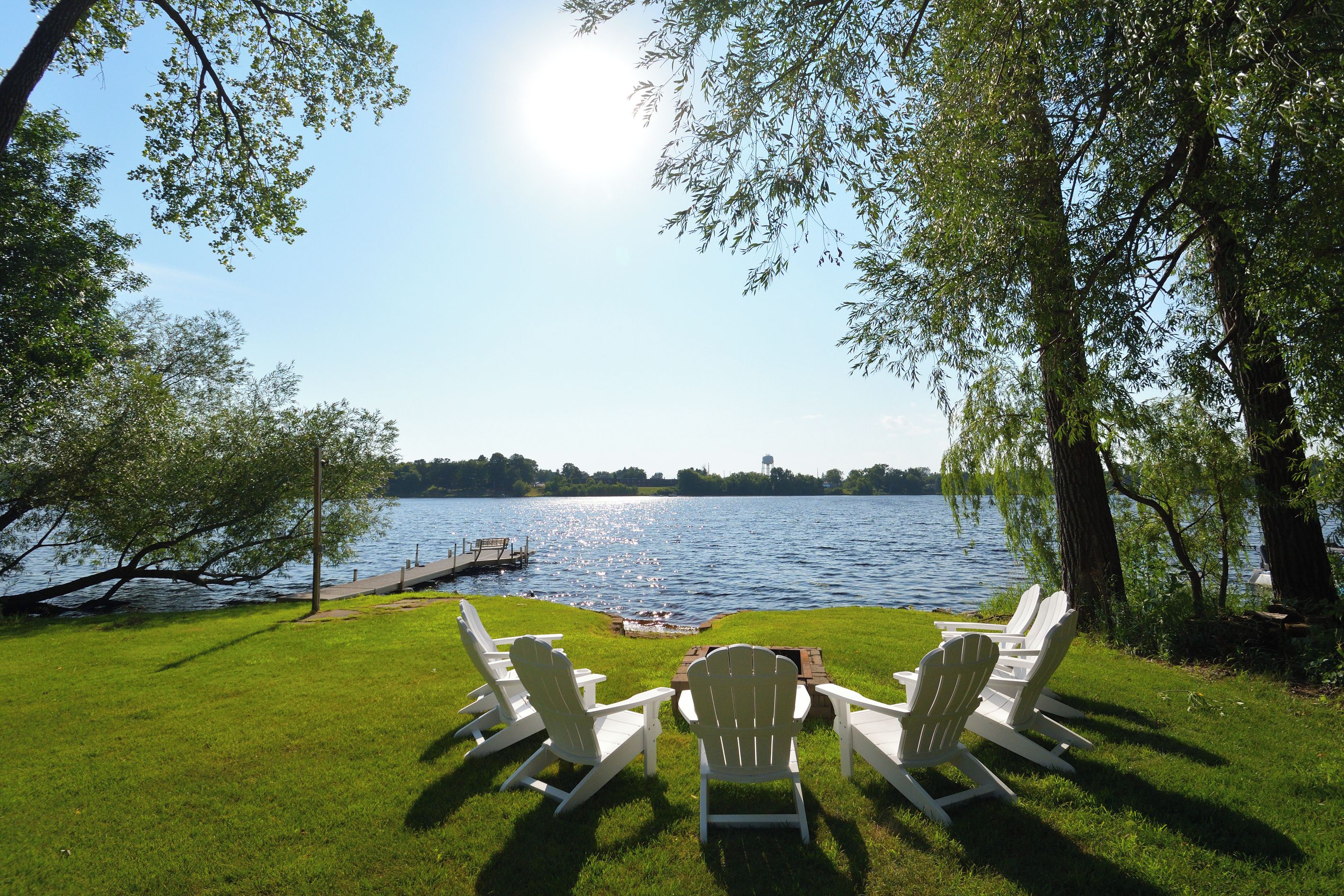 A lakeside view with a dock, chairs, and a grassy area.