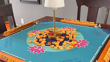 Mesa de Mahjong com peças e uma lâmpada no centro, rodeada por cadeiras.