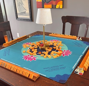 A Mahjong table with tiles and a lamp in the center, surrounded by chairs.